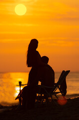 Fototapeta na wymiar Dreamy evening landscape on beach with silhouettes hugging couple with hookah during golden sunset