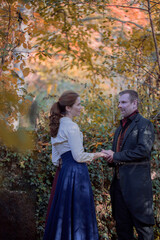 Vampire man wearing victorian suit with vampire woman in the autumn forest. Vintage medieval concept style.