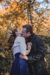 Vampire man wearing victorian suit in the autumn forest bites a woman. Vintage medieval concept style.