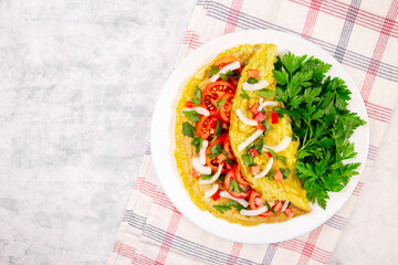 Omelet with parsley and tomatoes in a pan on a gray background, top view