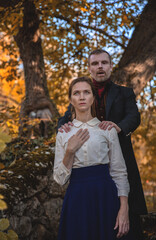 Vampire man wearing victorian suit with vampire woman in the autumn forest. Vintage medieval concept style.