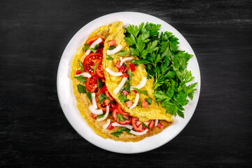Omelet with parsley and tomatoes in a pan on a black background, top view