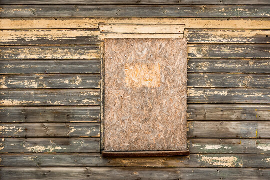 An old wooden window boarded up with plywood on a wooden wall