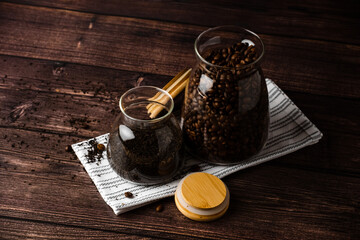 Storage of coffee and tea in glass jars. Glass jars with wooden lids filled with coffee beans and tea leaves stand on a table against a dark background.