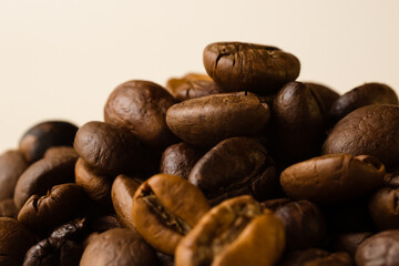 A bunch of coffee beans on a beige background. Side view, macro.