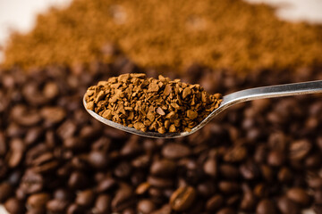 A spoonful of instant coffee against the background of a cluster of coffee beans and a scattering of instant coffee.