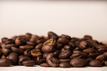 A bunch of coffee beans on a beige background. Side view. Macro