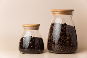 Storage of coffee and tea in glass jars. Glass jars with wooden lids filled with coffee beans and tea leaves stand on the table on a light beige background.