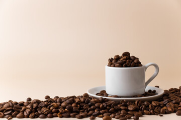 Espresso cup filled with coffee beans surrounded by a large number of coffee beans on a light beige background close-up.