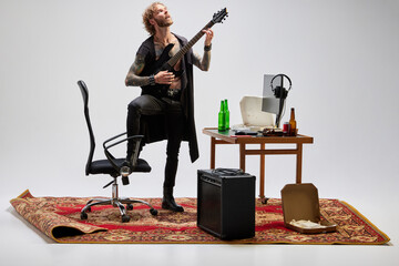 Stylish man, rock musician sitting at home and playing guitar. Retro, vintage style. Music,...