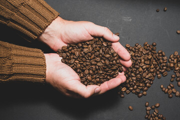 Male hands hold coffee on a dark background.
