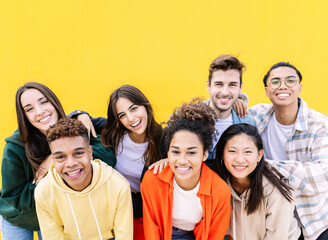 Group portrait of young multiethnic student friends against yellow wall - Diverse united millennial boys and girls smiling at camera outdoors - International youth community people concept