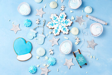 Preparation for celebrating merry christmas. Gingerbread in the form of mittens and snowflakes, christmas tree decorations, marshmallows and meringues in white and blue colors. View from above.