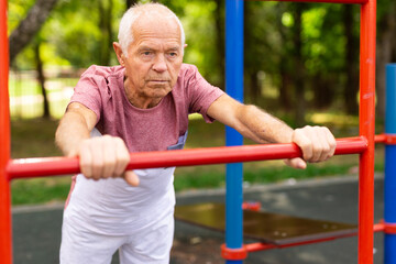 Obraz premium Elderly man doing fitness on sports ground equipment in park