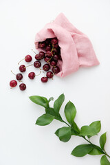 Ripe cherry in a pink linen bag on a white background, near a green branch. Practical use of reusable cloth bags for berries. Zero waste and sustainable plastic free lifestyle. 