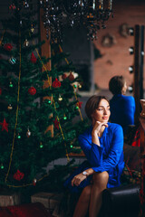 Woman in beautiful dress sitting by Christmas tree