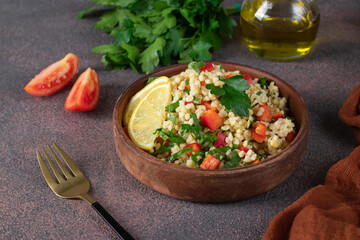 Traditional oriental salad Tabouleh with bulgur and parsley on brown background