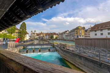 Naklejka premium LUCERNE, SWITZERLAND, JUNE 21, 2022 - Small waterfalls of Reuss river with historic buildings on the background in the center city of Lucerne, Switzerland