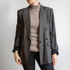 Woman wearing oversized grey blazer, beige turtleneck and black skinny jeans isolated on white...