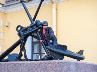A little boy taking pictures next to the sights of St. Petersburg. A child standing near a huge anchor in St. Petersburg