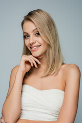 happy blonde woman with bare shoulders and natural makeup looking at camera isolated on grey.