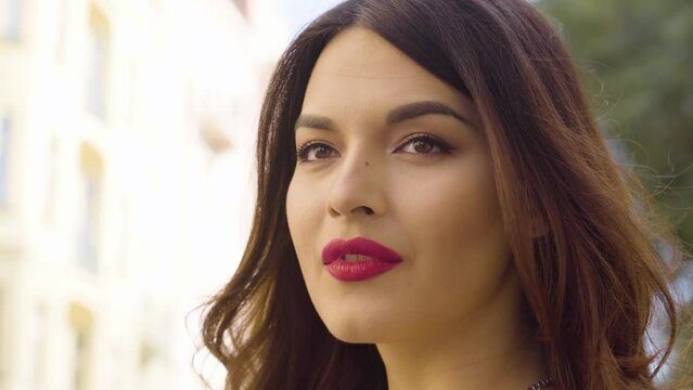 A young beautiful Caucasian woman looks into distance with a smile, then at the camera and laughs in an urban area - closeup