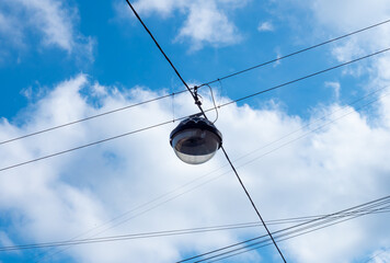 Black round glass pendant lamp hanging in the at the crossing of black electrical wires over city road against the blue sky