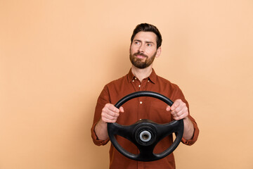 Portrait of minded positive man arms hold wheel look interested empty space isolated on beige color...