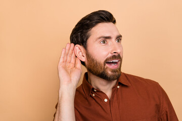 Portrait of positive cheerful man arm near ear listen interested eavesdrop isolated on beige color background