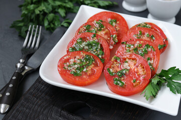 Vegetarian appetizer of tomatoes with garlic, parsley, dressed with honey and olive oil in plate on gray background, Closeup
