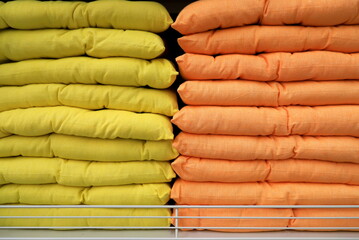 Pillows are stacked on shelf. Pillows background. Soft comfortable orange and yellow Household items for home bedroom, bed furniture, indoors