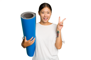Young asian woman holding a mat isolated on green chroma background joyful and carefree showing a peace symbol with fingers.