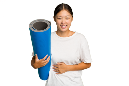 Young asian woman holding a mat isolated on green chroma background laughing and having fun.
