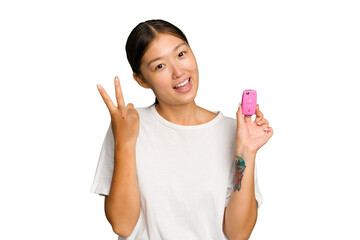 Young asian woman holding car keys isolated on green chroma background joyful and carefree showing a peace symbol with fingers.