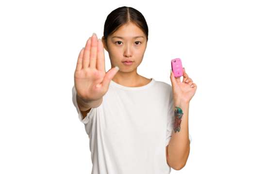 Young asian woman holding car keys isolated on green chroma background standing with outstretched hand showing stop sign, preventing you.