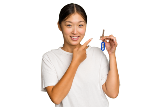 Young asian woman holding home keys isolated on green chroma background smiling and pointing aside, showing something at blank space.