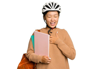 Young student asian woman wearing a bike helmet isolated on green chroma background laughs out loudly keeping hand on chest.