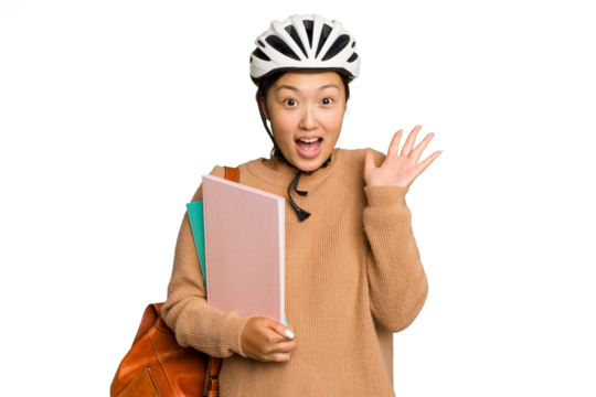 Young student asian woman wearing a bike helmet isolated on green chroma background receiving a pleasant surprise, excited and raising hands.