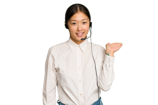 Telemarketer asian woman working with a headset isolated on green chroma background showing a copy space on a palm and holding another hand on waist.