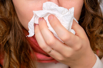 Fototapeta premium A sick woman blows her nose in a napkin, a runny nose. Adult ill woman with a red scarf, female aged 35 years
