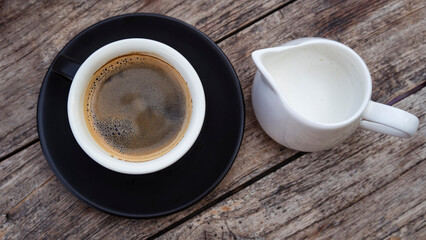 A cup of hot coffee and milk jug. Cozy breakfast in the cafe.