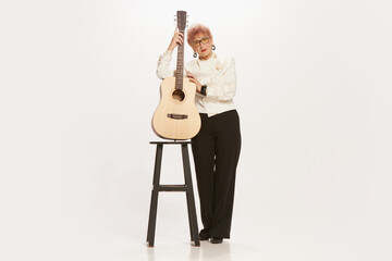 Naklejka premium Studio shot of elegant senior woman in retro vintage style outfit posing with guitar isolated on white background. Concept of beauty, music, fashion, emotions