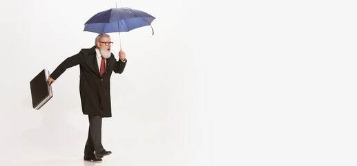 Portrait of active senior man in retro vintage black coat walking with umbrella isolated on white background. Concept of beauty, old generation, fashion, emotions