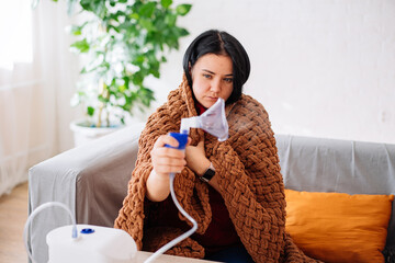 a young woman holding a steam nebulizer inhaler in her hand, treats flu and asthma from the bronchitis virus at home.