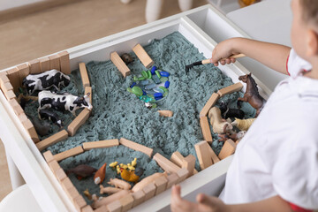 Cute baby boy playing sensory box kinetic sand table with farm animals