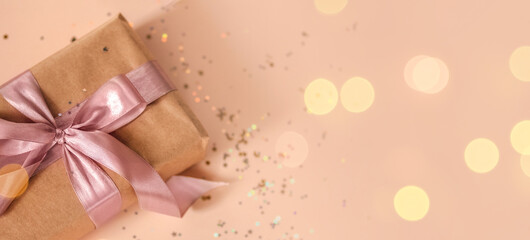 Valentines Day, Birthday or New Year present in kraft paper with pink ribbon on soft beige background with glitter and bokeh. Happy holidays celebration and giving love concept. 2022 2023 Xmas, top 