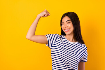 Photo of positive adorable girl toothy beaming smile arm demonstrate biceps isolated on yellow...