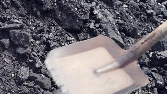 Man picks up coal with a shovel. Energy and fuel industry. Volcanic rock.