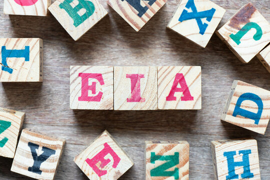 Alphabet letter block in word EIA (abbreviation of Environmental Impact Assessment) and another letter on wood background
