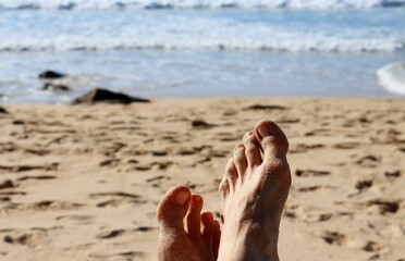 Women's feet in the sand against a backdrop of beach and ocean. Lazy relaxation on the beach.  